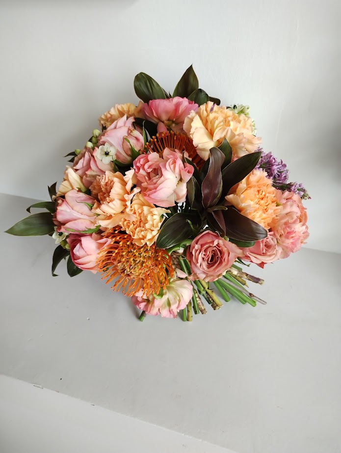 White and pastel flowers arranged as a wedding centerpiece on a rustic wooden table in a softly lit reception hall with a romantic and elegant atmosphere